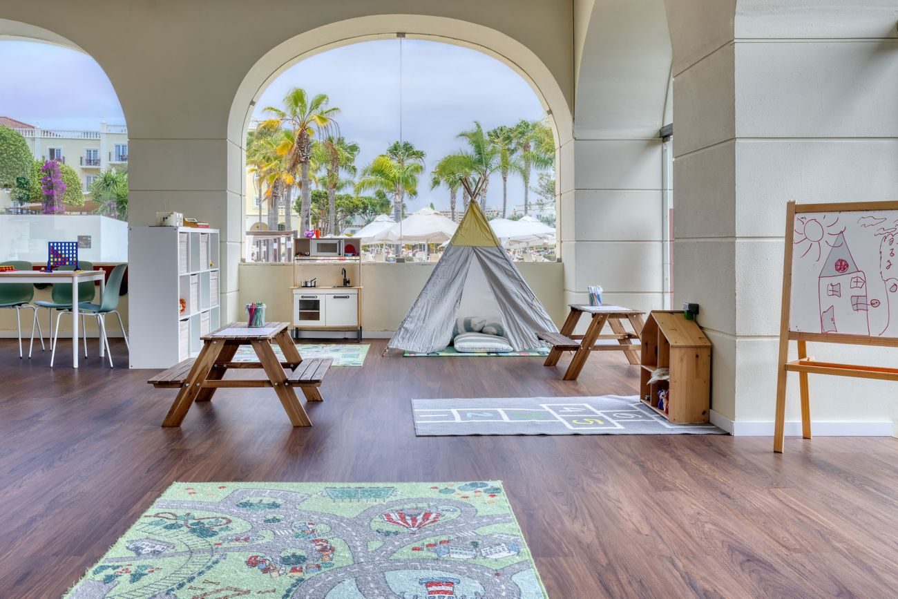 The Kiepos kids' room at Domes Lake Algarve — a teepee, small picnic tables, a toy kitchen and an easel, opening through arches onto palm trees.