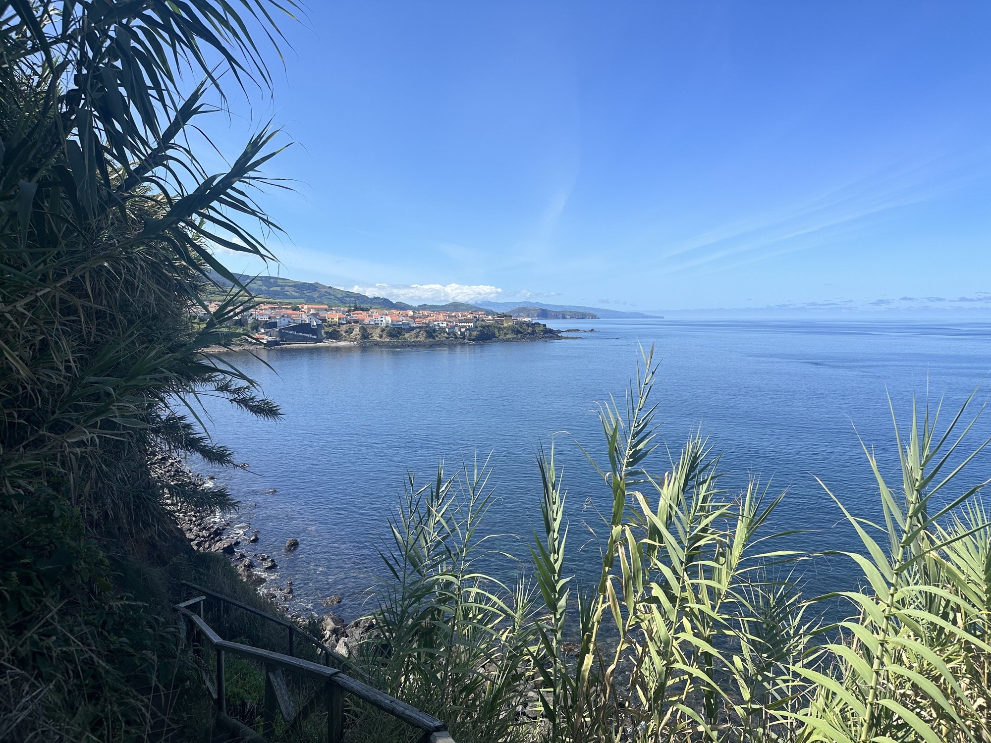 A blue bay with a small red-roofed village on the headland in the Azores.