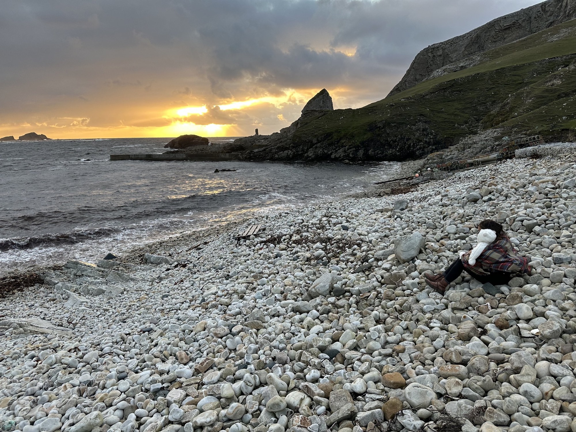 Sunset over a pebble beach and sea cliffs on a rugged coastline.