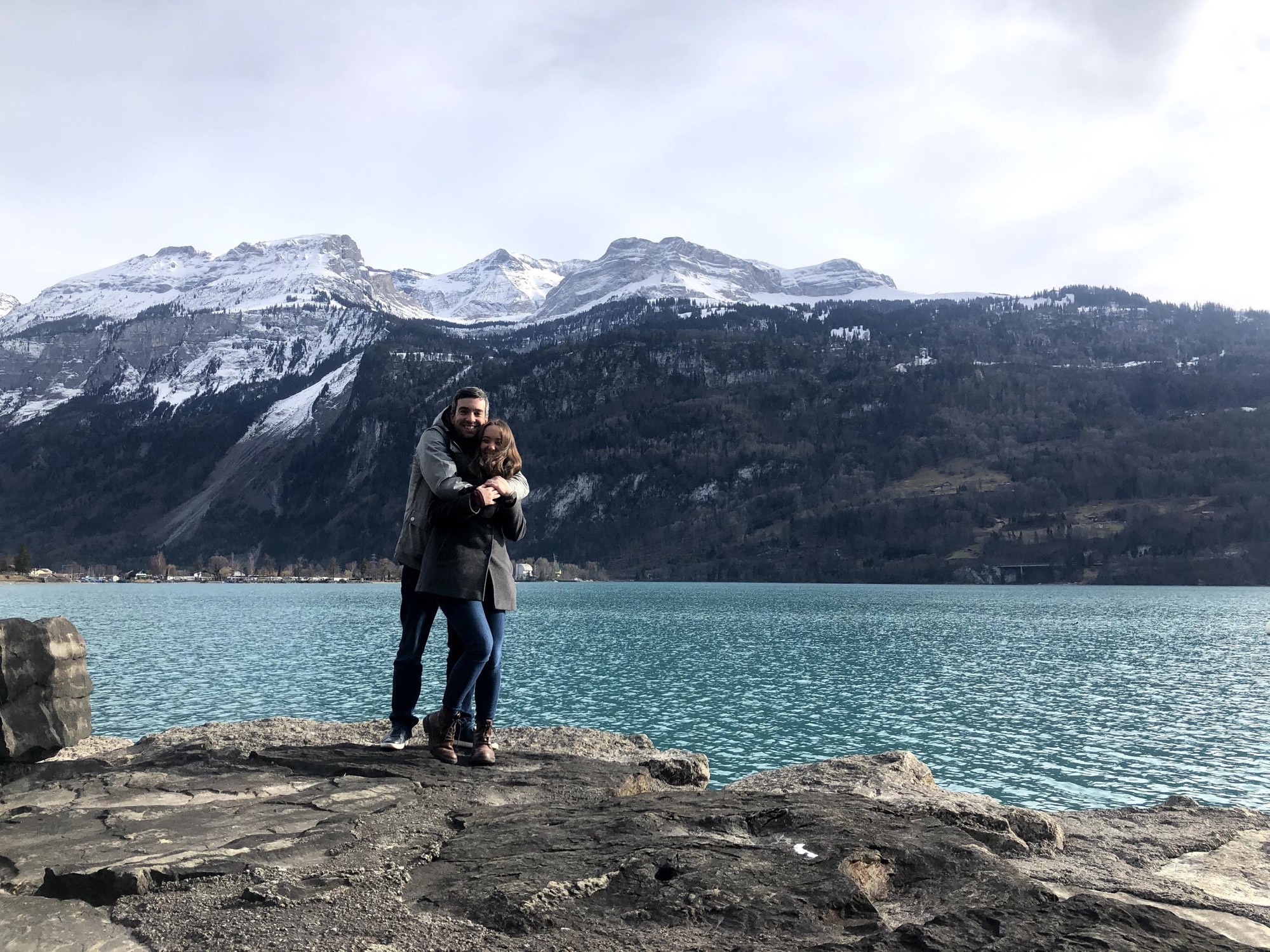 Brittany and her husband on a rocky shoreline in front of a snow-capped mountain range in Switzerland.