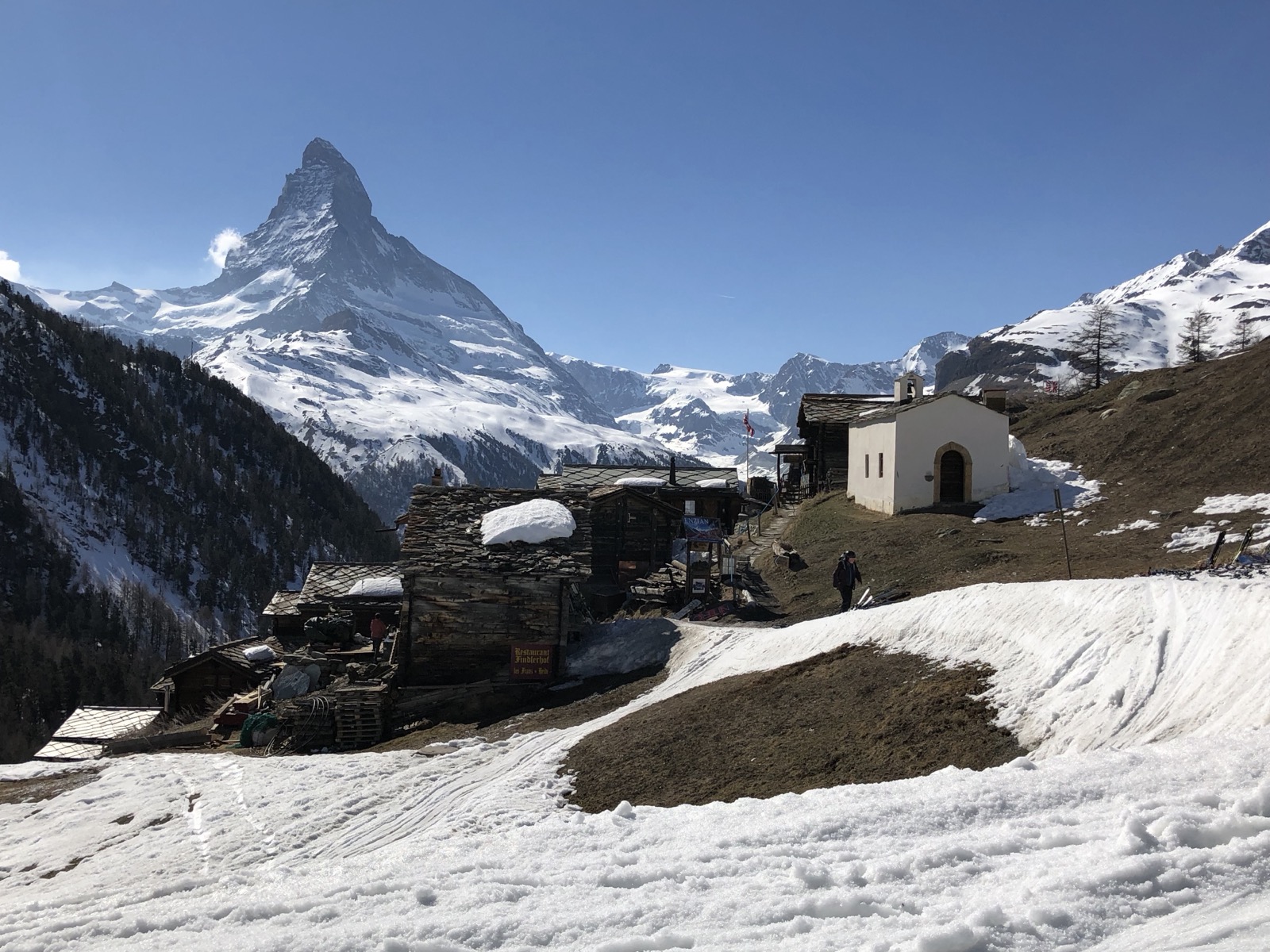 The hamlet of Findeln above Zermatt, old wooden huts and a small white chapel with the Matterhorn behind, in late-season snow.