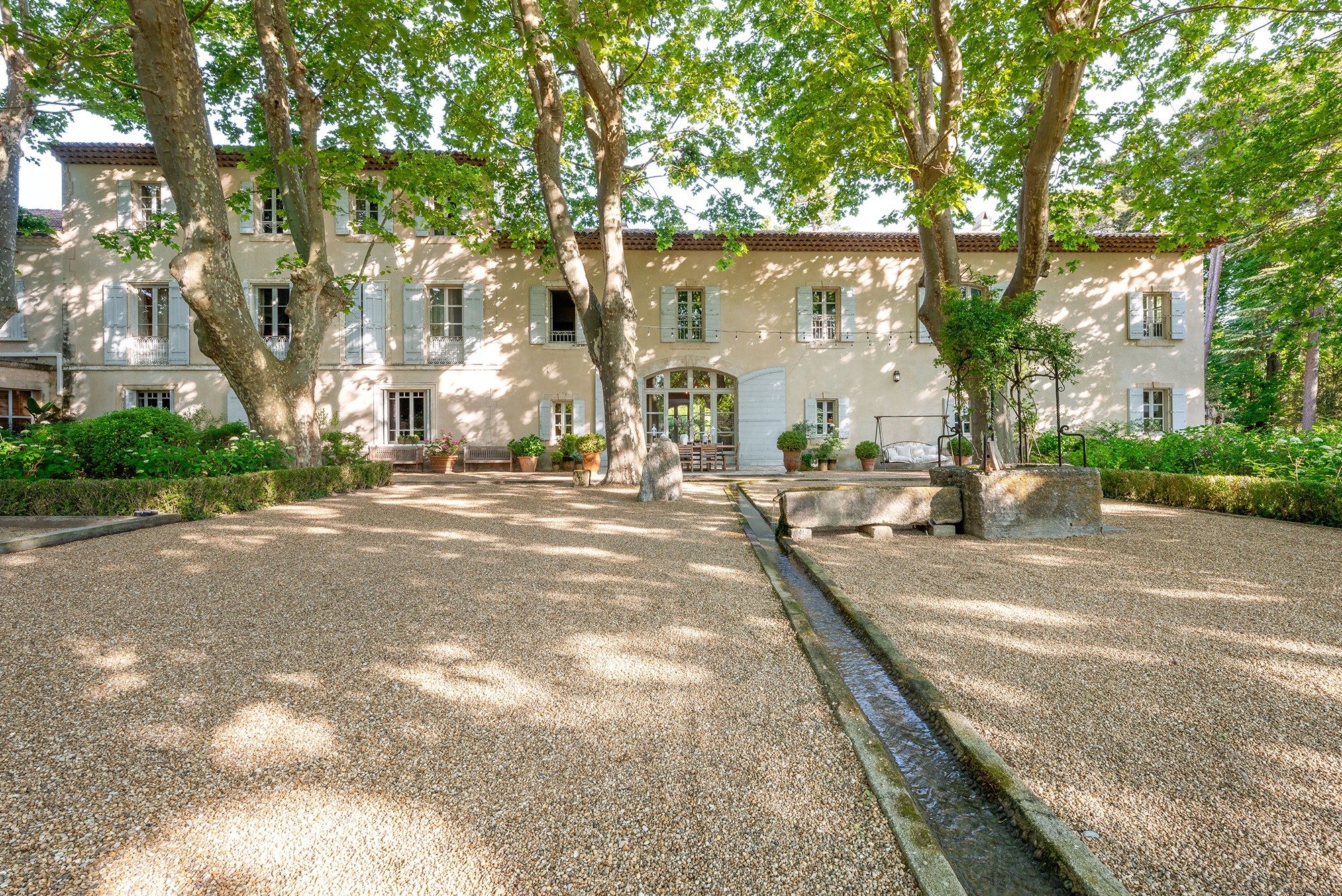 A stone farmhouse in Provence behind plane trees, with a gravel courtyard.